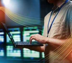 IT specialist using a laptop to monitor networking systems in a data center